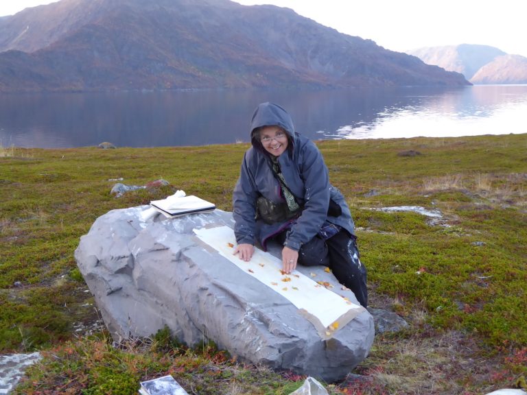 Frances working on a long painting laid over a rock beside the fjord at Alta, Norway